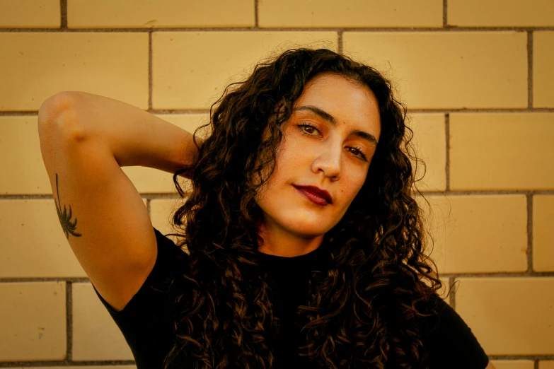 a woman with long hair and tattoos stands against a brick wall