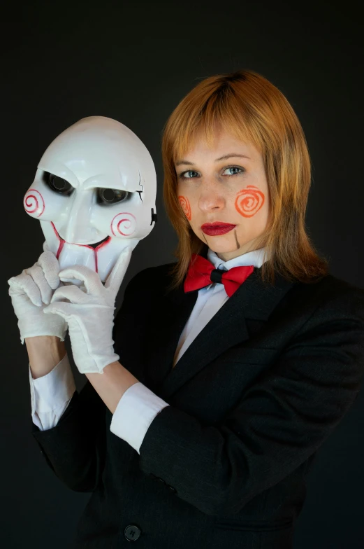 a woman holding a white mask that has been decorated to look like a human face