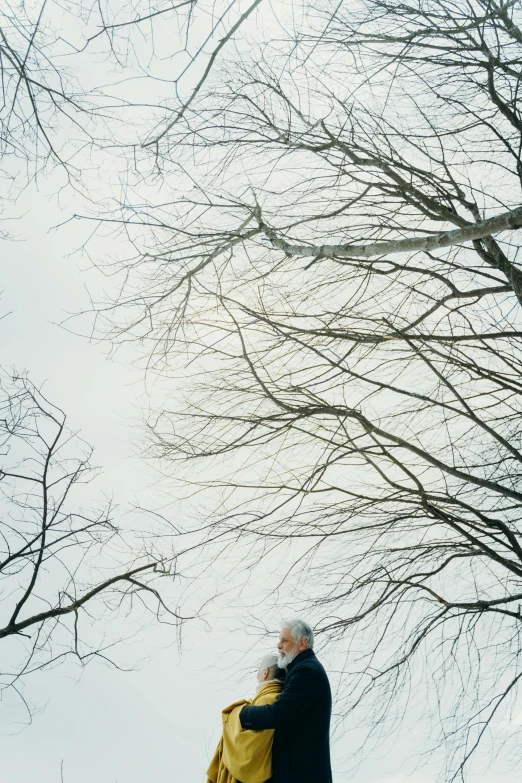 a man in a blue jacket standing next to trees with no leaves