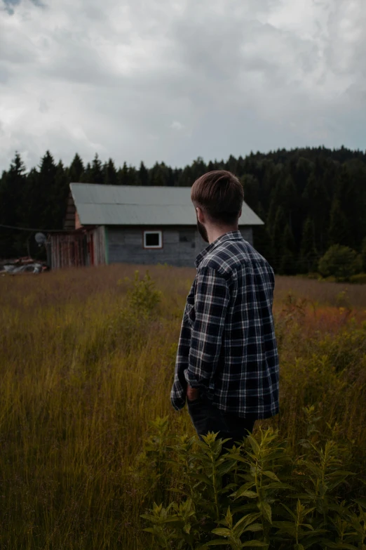 young man standing in the grass with his back turned to the camera