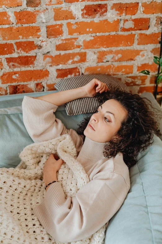 a woman laying on a bed in front of a brick wall