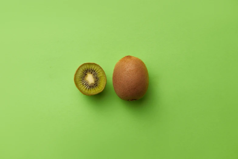 a kiwi slice and half of an orange on green background