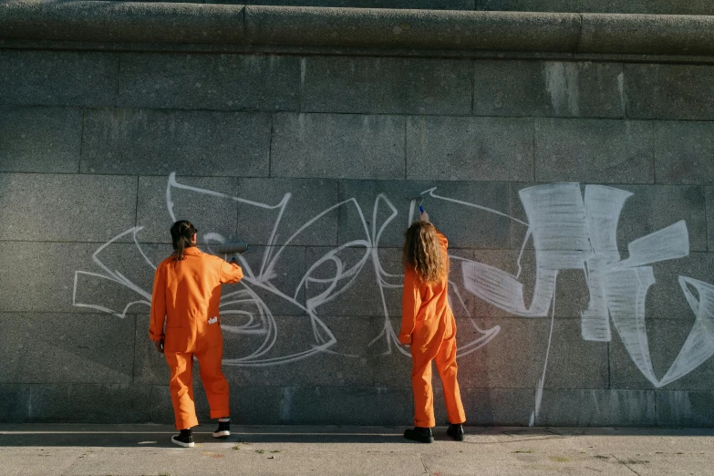 two s standing on a sidewalk by graffiti