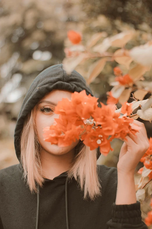 a girl in black jacket holding flowers in a tree