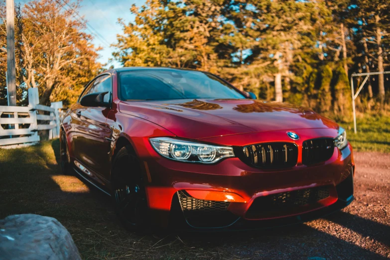 the red bmw is parked in front of a white fence