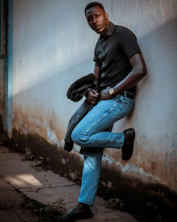 a man leaning against a wall with his pants on