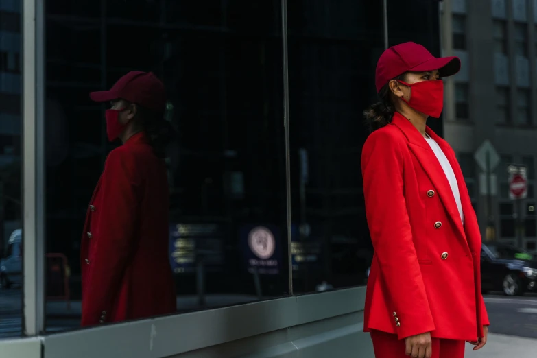 a woman in a red outfit and hat in front of a window with a face mask on