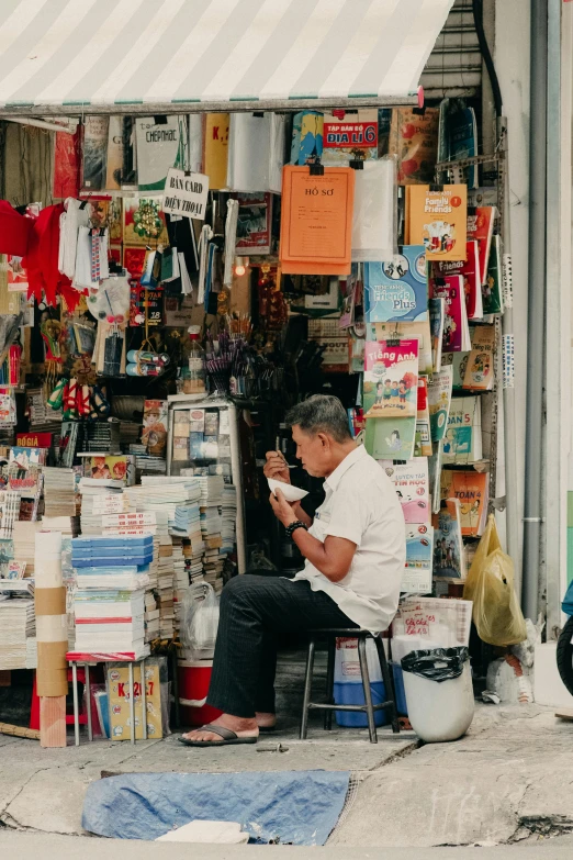 a man sitting outside in front of a store selling stuff