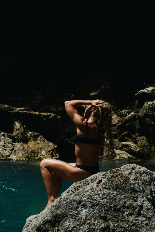 a woman in a bikini standing on top of a large rock