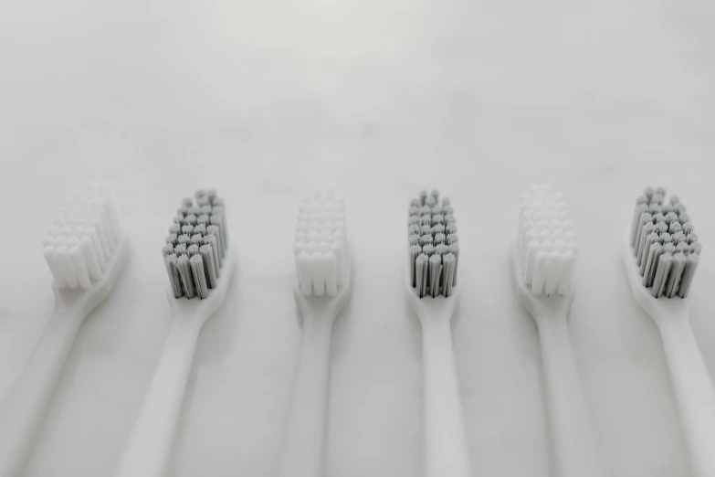 five white toothbrushes lined up in rows on a white surface