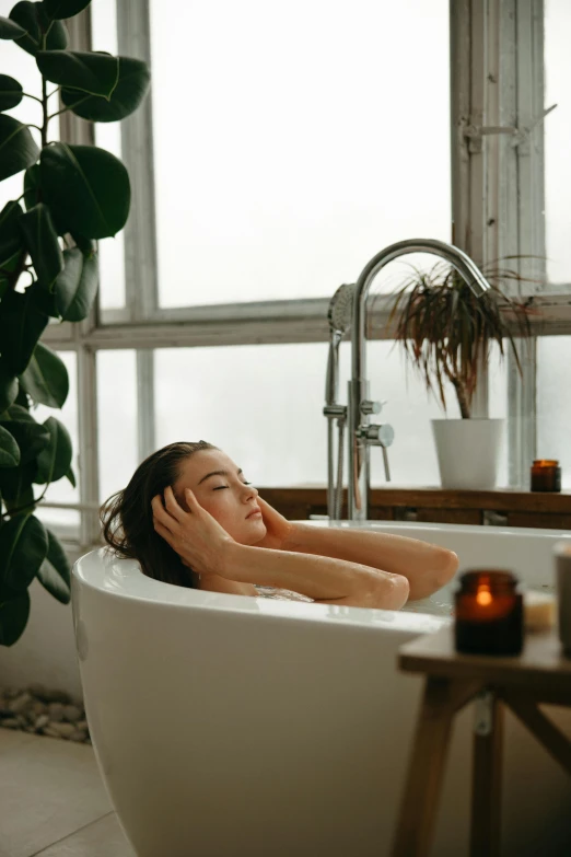 woman with hand on head lying in bath tub in bathroom