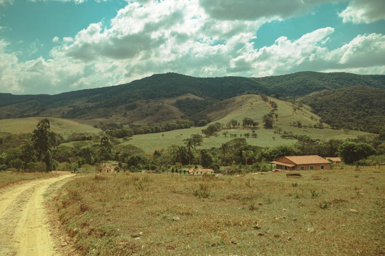 a dirt road next to the grass with a hill in the background