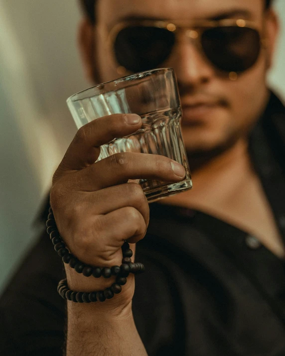 a man with dark sunglasses holding a glass