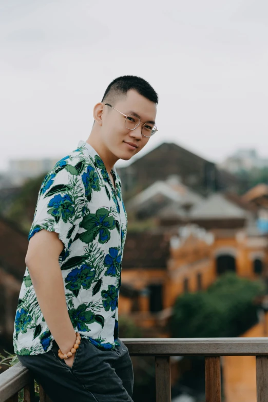 man posing by a railing, wearing glasses