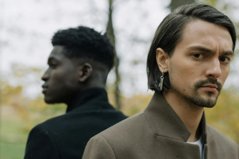 two men wearing brown jackets one wearing earrings