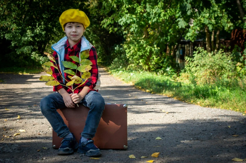 a boy sitting on top of a brown suitcase