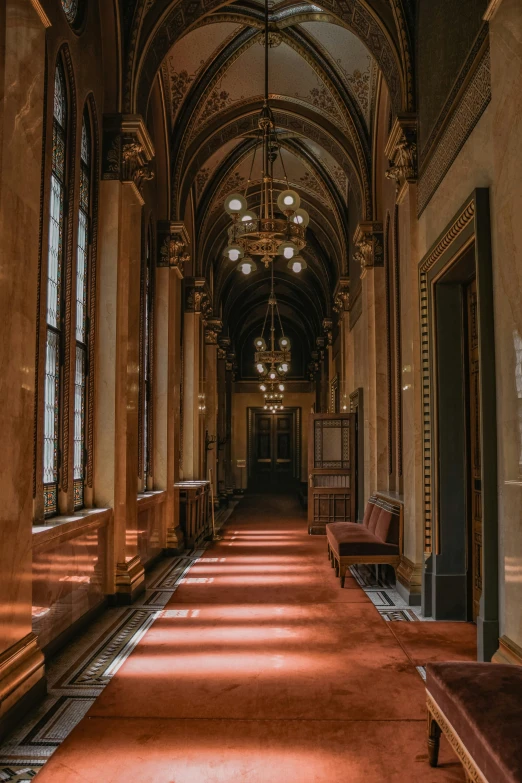 the long corridor is decorated with fancy ceiling, chairs and chandeliers