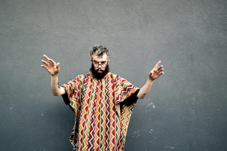 man wearing large hand made colorful t - shirt posing in front of gray wall