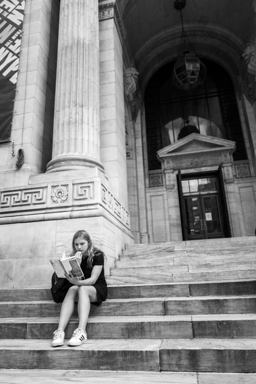woman sitting on stairs reading a book in front of an old building