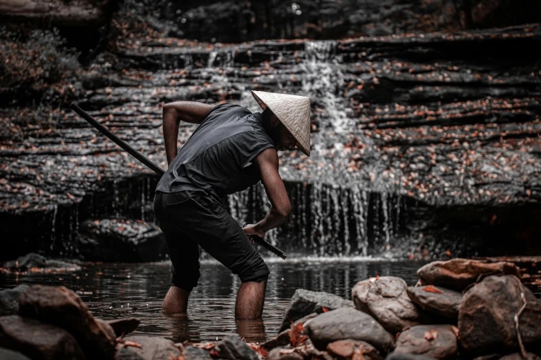 a man with a stick stands by a waterfall