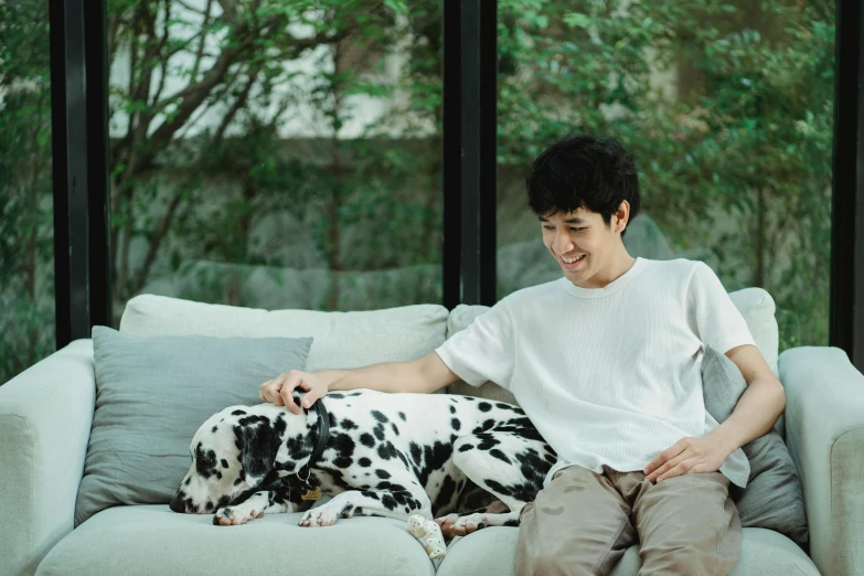 the young man sitting on a couch has a black and white dog resting next to his feet