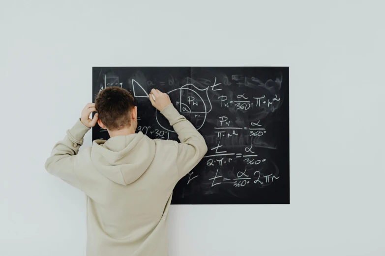 man writing on blackboard with white walls