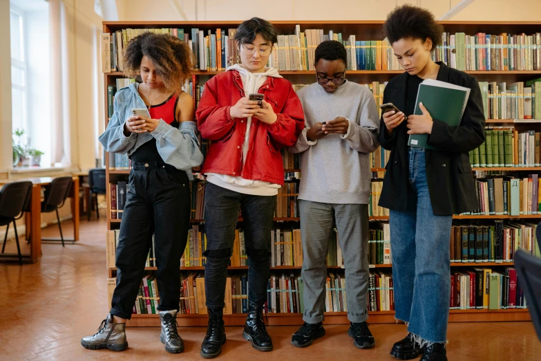 four young women look at their phones in front of a liry