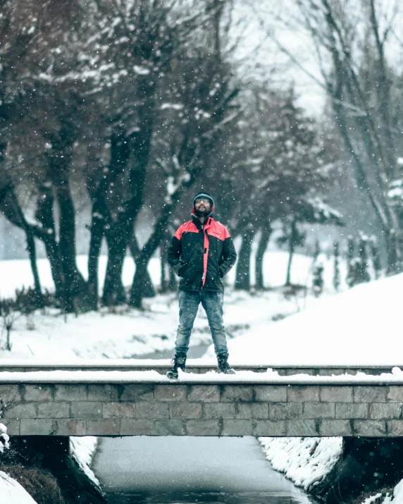 a man standing on a bridge near a river in winter