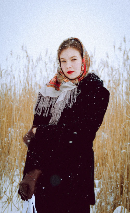 a woman standing in the snow by some tall grass