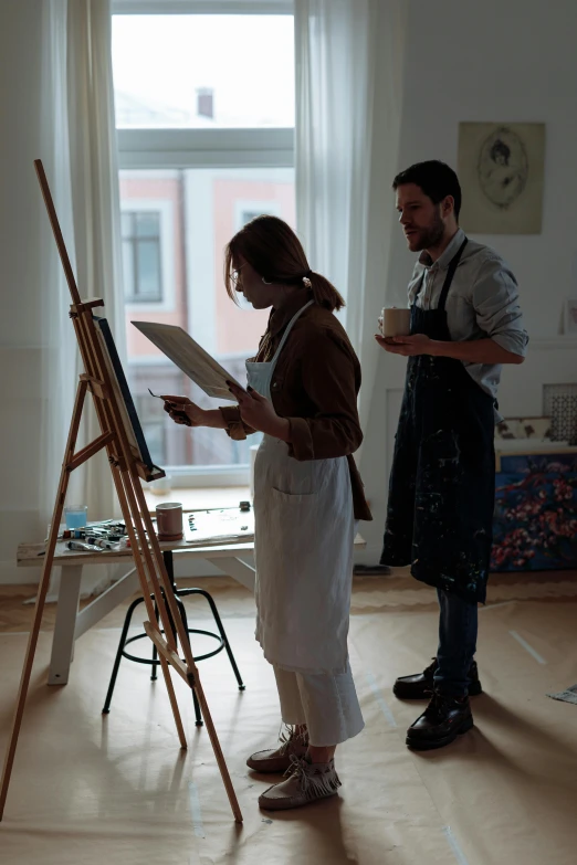 two people standing in a white room while holding a black and white easel