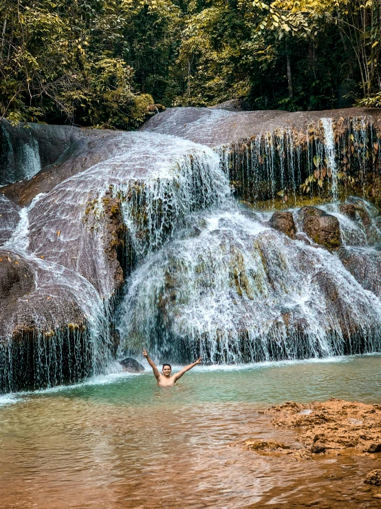 a man swimming in the river below a waterfall