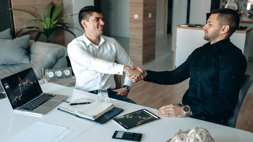 two men sitting at a desk shaking hands