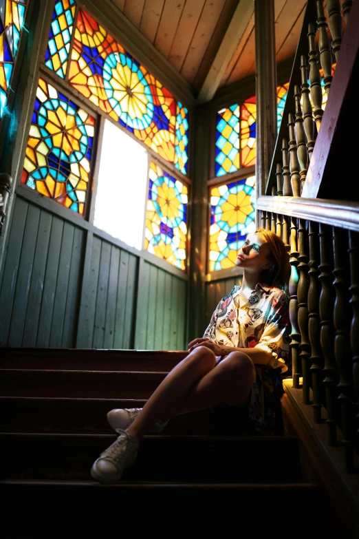 woman in floral print dress sitting on stairs with stained glass windows behind her