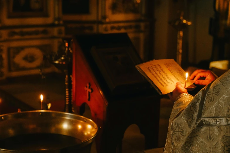 the priest holds the bible as he lights candles in his altar