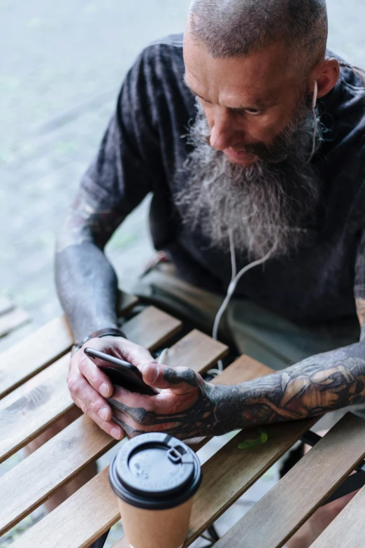 the tattooed man is using his phone while sitting on the bench