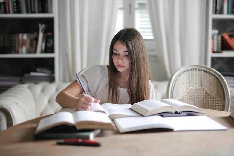 a girl is writing while sitting at a table with a book