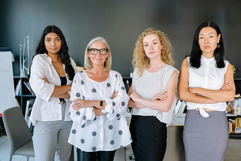 three women standing in an office with their arms crossed