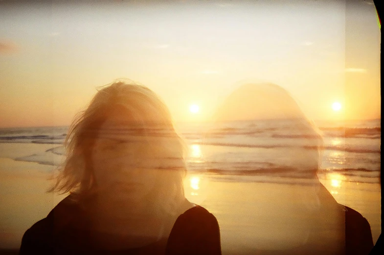 two women standing on a beach with the sun behind them