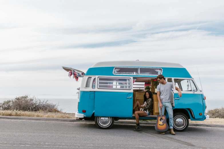 an old blue van with a guitar strapped to it is parked with two people