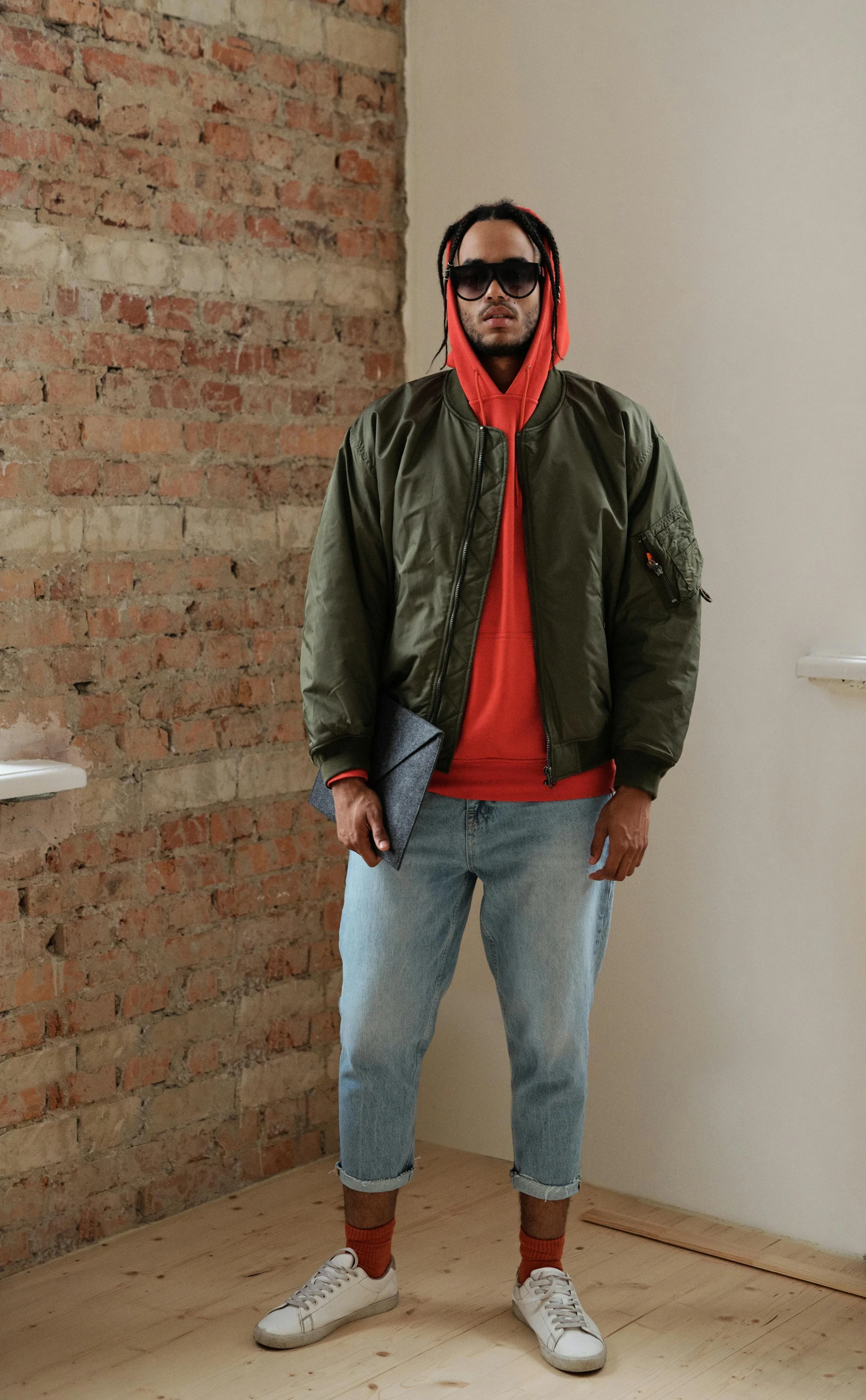 a man standing next to a brick wall wearing a hood