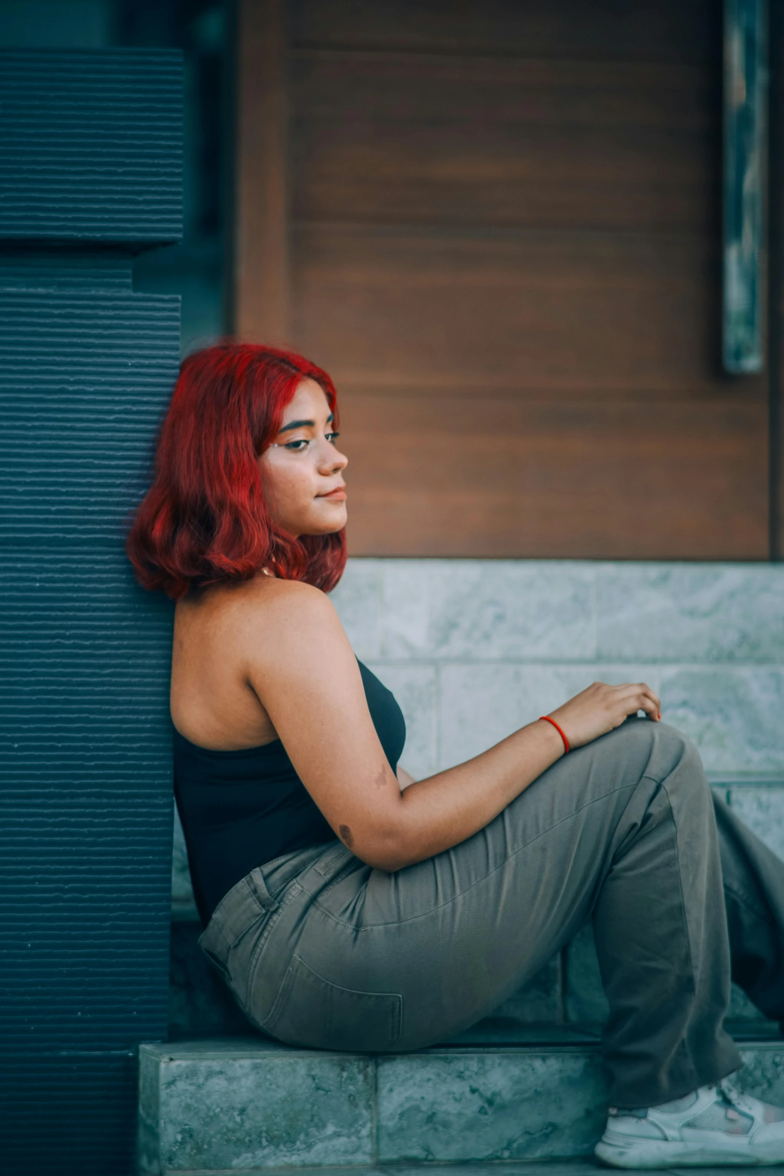 a woman wearing a tank top and brown pants sitting down