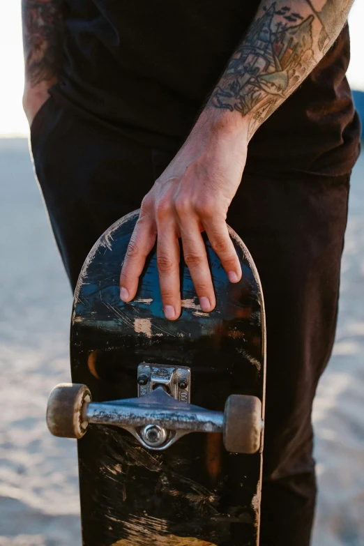 a person holds a skateboard while standing by the water