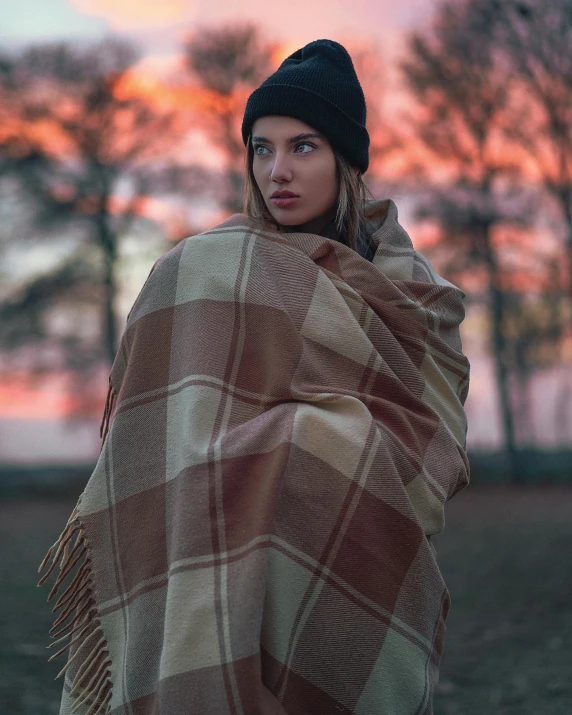 a woman wrapped in plaid blanket at dusk