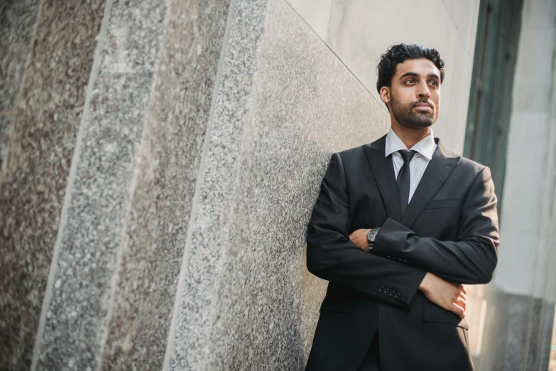 a man in a suit leans against the side of a building