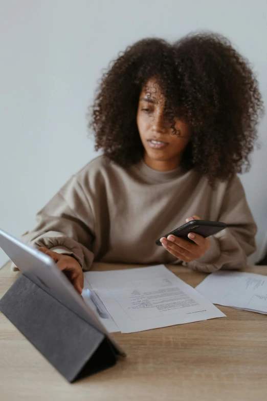 a woman sitting at a table using a phone while looking at papers