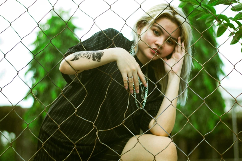 the young lady poses behind a fence with tattoos