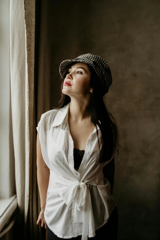 a woman in a hat is standing by a window