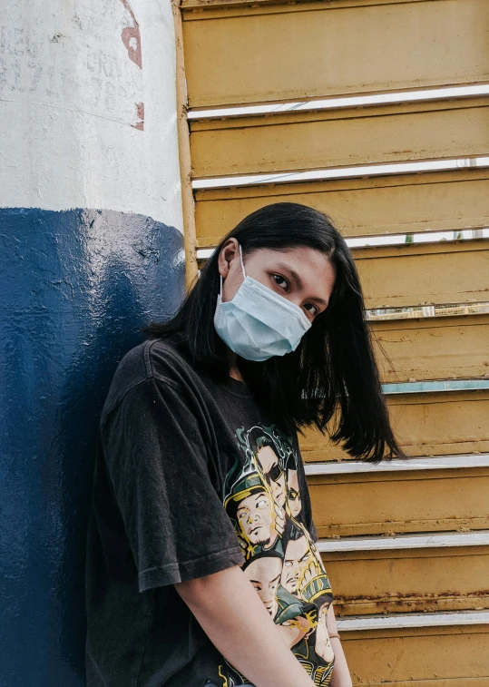 a woman wearing a mask and standing against a wall