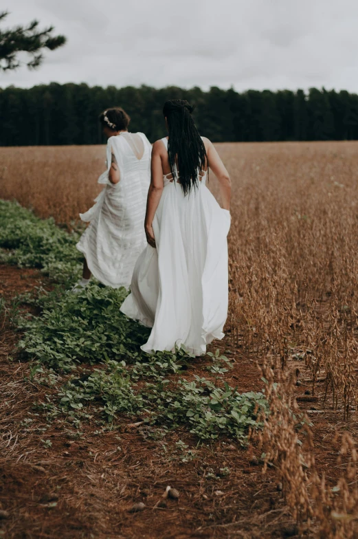 two women in dresses are walking across the grass