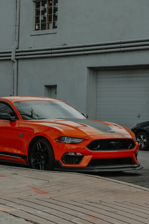 an orange and black mustang parked in front of a garage